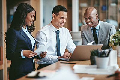 3 people sitting at desk looking at a laptop