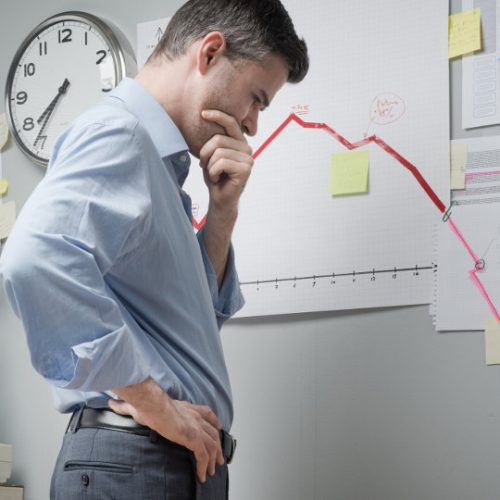 man looking disappointed next to a chart showing negative growth